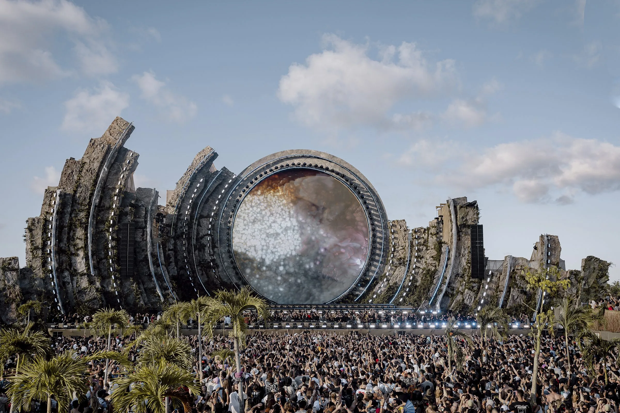 Crowd in front of a circular stage framed by rock structures and palm trees