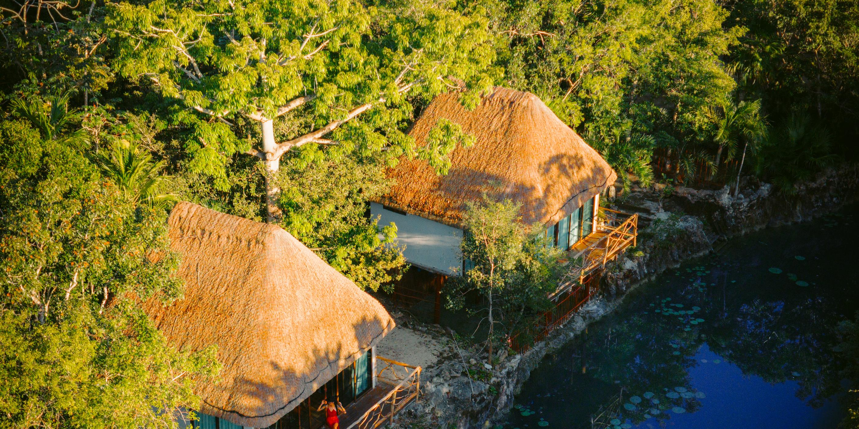 Aerial view of thatched cabañas beside a cenote in the Tulum jungle