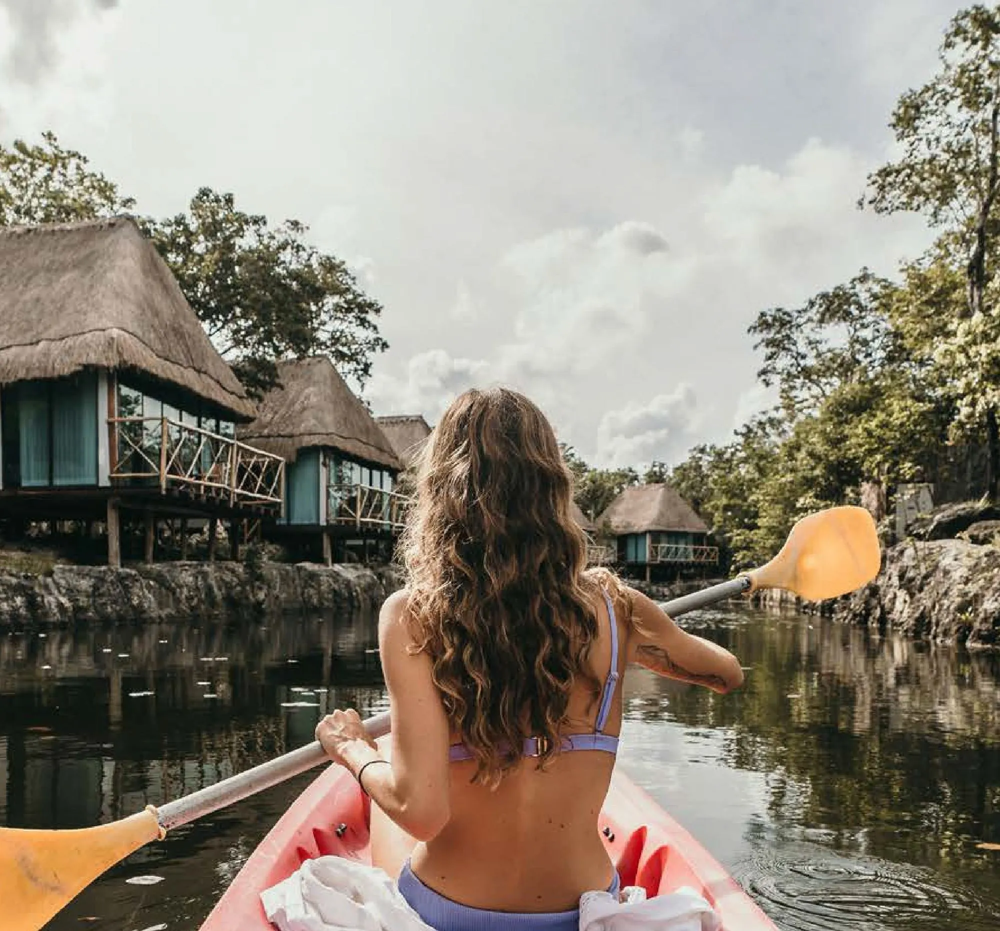 A guest kayaking past jungle cabañas in Tulum